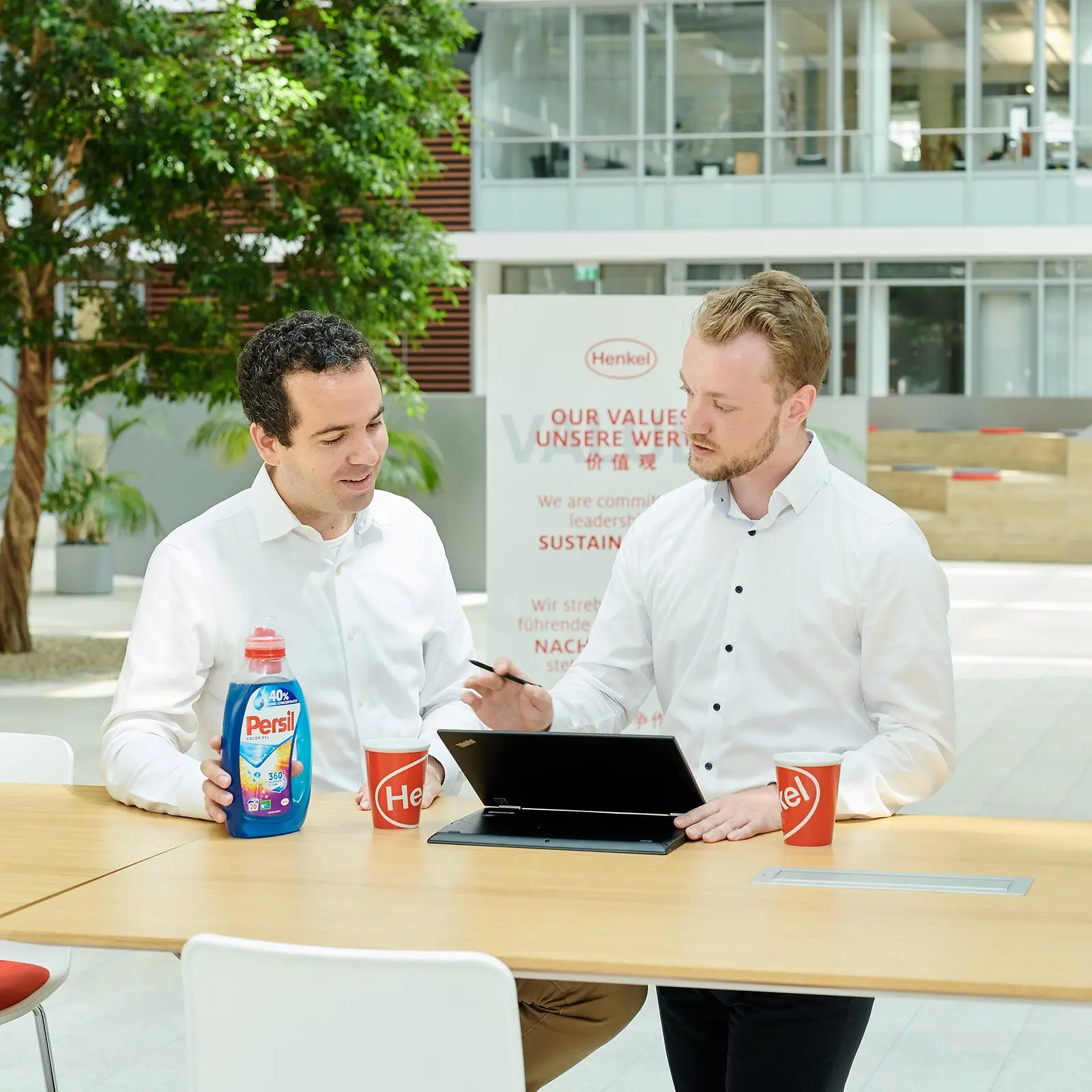 两位男子站在桌子前，拿着宝莹包装瓶和笔记本电脑