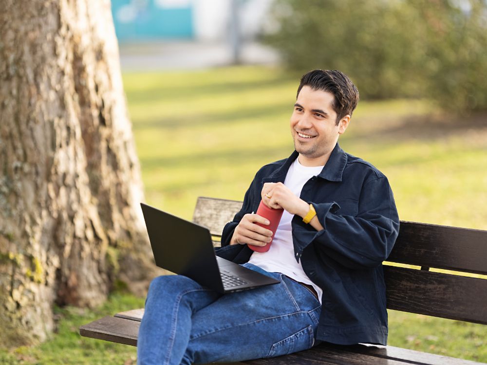 汉高的一名员工坐在公园的长凳上，用他的笔记本电脑工作。 