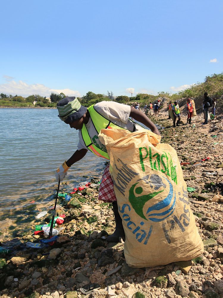 Woman collecting plastic waste on beach in Haiti